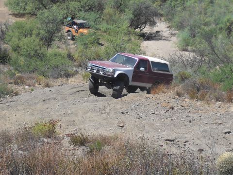 1986 Ford Bronco - This SUV, likely a 1987 Ford Bronco, navigates a dusty trail with a companion vehicle in the distance.
