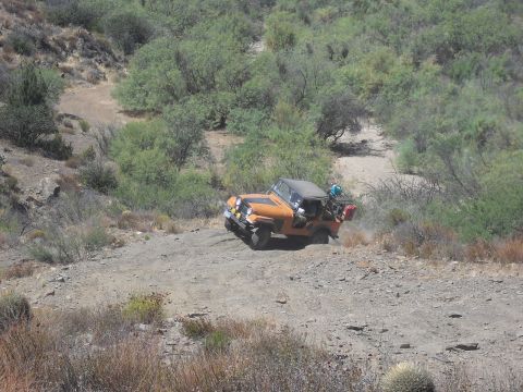 1986 Ford Bronco - A Jeep navigates a challenging off-road path, kicking up dust as it climbs.