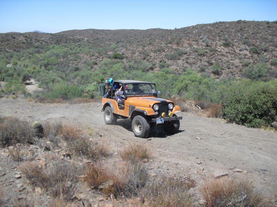 Orange Jeep CJ-7 driving on a dirt road, with luggage rack on back