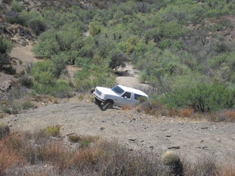 1986 Ford Bronco - A white 1987 Ford Bronco navigates a challenging dirt road in a , arid landscape.