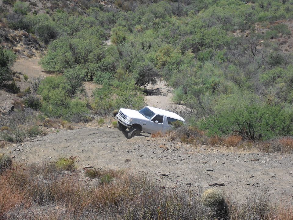 White 1987 Ford Bronco driving off-road on a dirt path