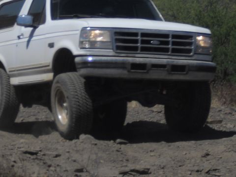 1986 Ford Bronco - This white SUV is captured from a low angle as it navigates a dirt path, its front grille and headlights.