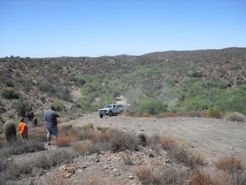 1986 Ford Bronco - 1986 Ford Bronco navigates a dirt track in a dry, hilly terrain under a clear blue sky.