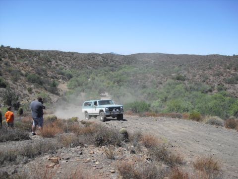 1986 Ford Bronco - A two-tone Chevrolet K5 Blazer navigates a dusty off-road trail under a clear blue sky.