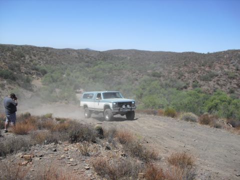 1986 Ford Bronco - A photographer captures a two-tone blue and white Ford Bronco as it kicks up dust on a remote dirt road.