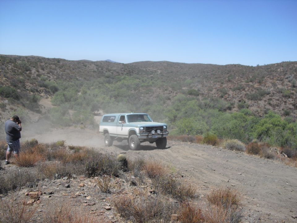 Two-tone blue and white Ford Bronco driving on a dusty dirt road