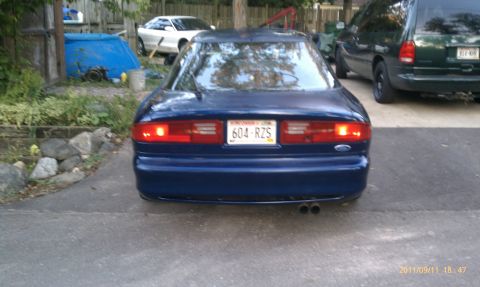 1994 Ford Probe - The rear of a blue 1994 Ford Probe is visible, parked in a driveway with other vehicles.