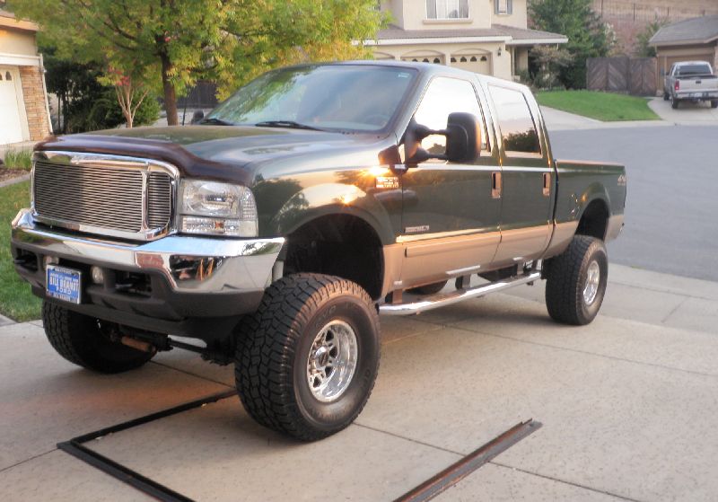 Green and tan 2002 Ford F-250 Super Duty pickup truck with chrome grille and wheels, lifted suspension, parked on a driveway