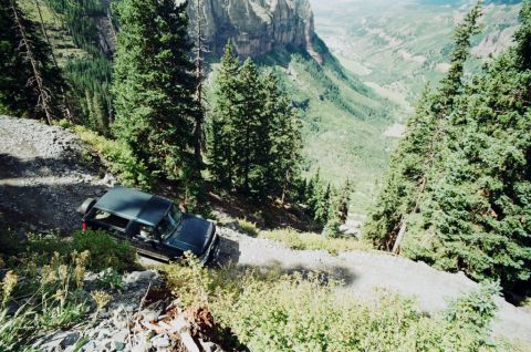 1995 Ford Bronco - A 1995 Ford Bronco navigates a challenging mountain trail, with a dramatic valley vista.