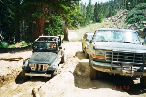 1995 Ford Bronco - A Ford Bronco and a Jeep navigate a rough, wooded trail.