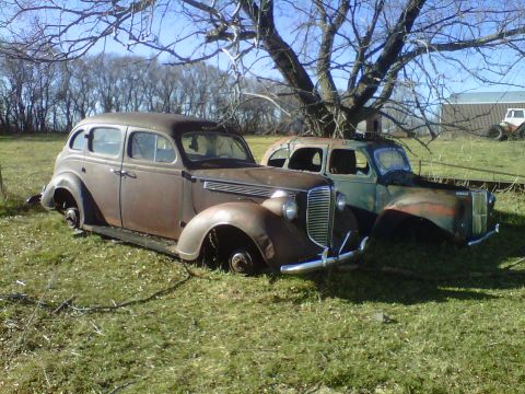 1978 Chevrolet C/K Pickup - Abandoned sedans rest in a field, their bodies weathered by time and the elements.