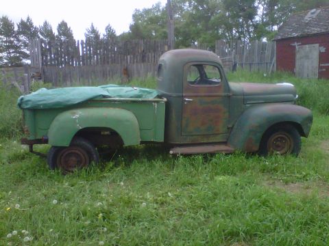 1978 Chevrolet C/K Pickup - This vintage green pickup truck sits in tall grass, with a tarp covering its bed and a weathered wooden fence in the background.