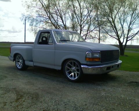 1978 Chevrolet C/K Pickup - A gray pickup truck sits on a dirt road, its custom wheels and lowered stance evident under a cloudy sky.