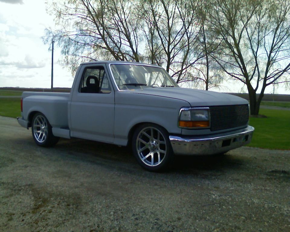 Gray pickup truck with aftermarket wheels, lowered suspension, and custom grille, viewed from the front three-quarter angle
