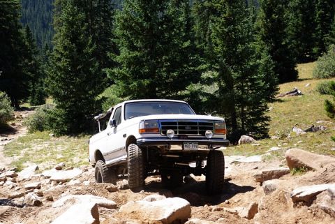 1995 Ford Bronco - 1995 Ford Bronco tackling an off-road trail in a mountainous, wooded area.