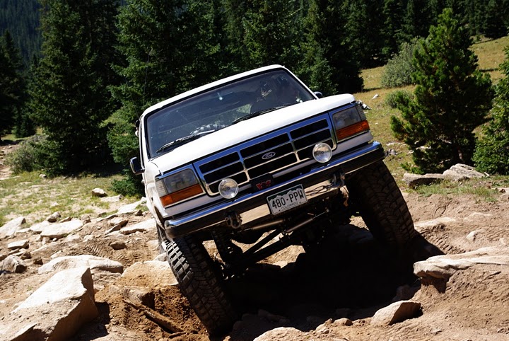 White Ford Bronco climbing a rocky alpine trail, front end flexed over boulders