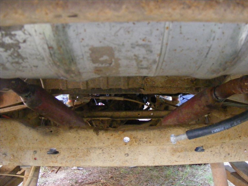 Undercarriage view of a rusty vehicle frame with fuel tank and exhaust pipes