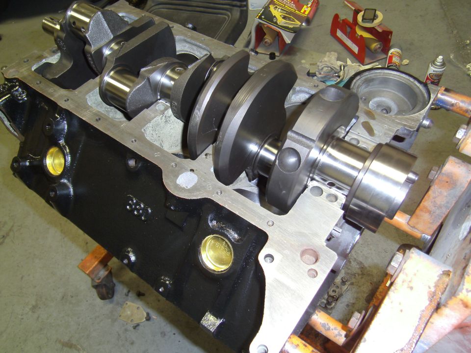 Engine block with crankshaft installed, sitting on an engine stand. Tools and parts are visible in the background
