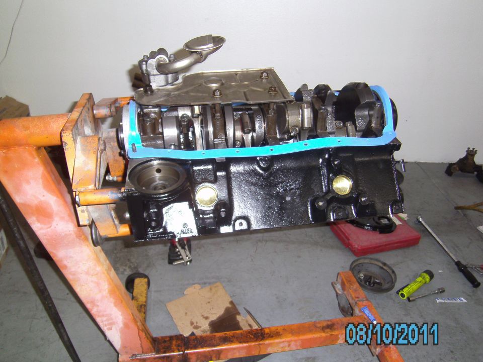 Engine block on an orange engine stand, with crankshaft and oil pump visible. Blue gasket installed