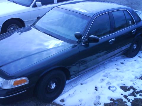 1998 Ford Crown Victoria - A dark 1998 Ford Crown Victoria sedan is parked in the snow next to another vehicle.