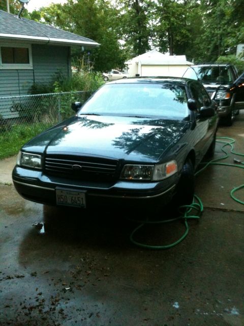1998 Ford Crown Victoria - A 1998 Ford Crown Victoria is parked in a driveway, with a hose nearby. Another vehicle is visible behind it.