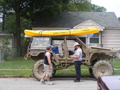 1978 Ford Bronco - A heavily modified off-road vehicle, possibly a Jeep, is parked on a residential street with two kayaks strapped to its roof.