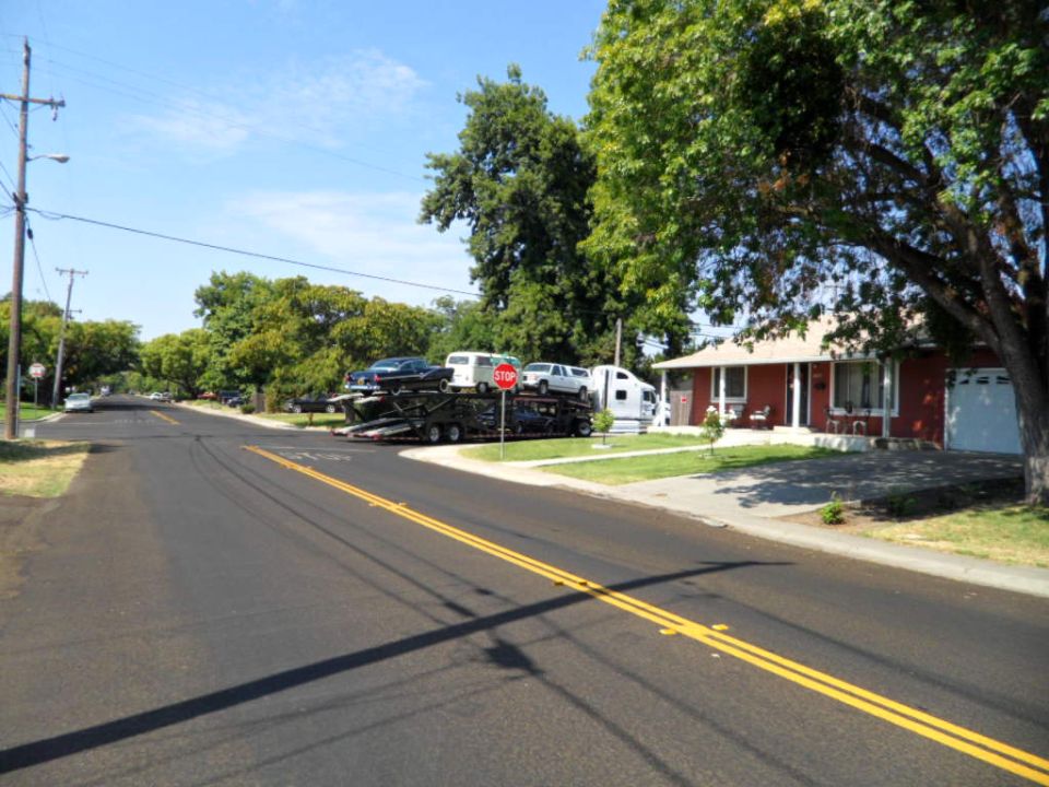 Car carrier truck loaded with a dark sedan, a white van, and another white vehicle, parked on a residential street