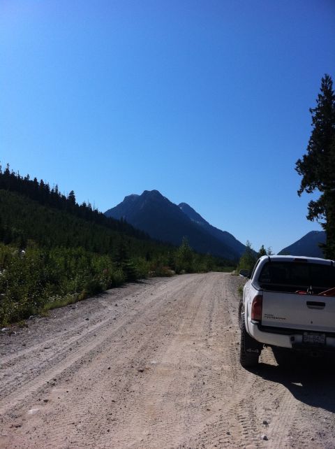 1990 Ford Bronco - A white pickup truck is parked on a dirt road, with a mountain range visible in the distance under a clear blue sky.