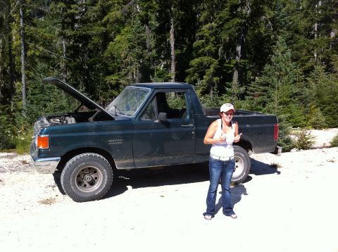 1990 Ford Bronco - A woman stands next to a dark green 1990 Ford Bronco with its hood open, giving a thumbs up.