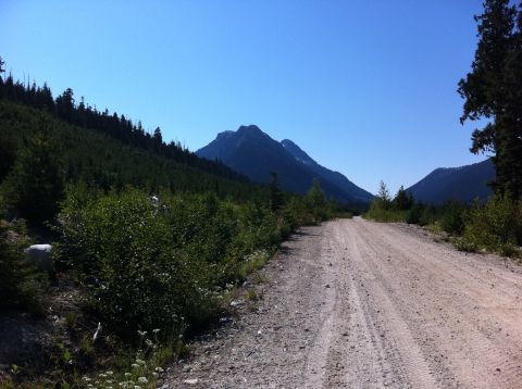 1990 Ford Bronco - A dirt road winds through a lush green valley towards distant mountains on a sunny day.