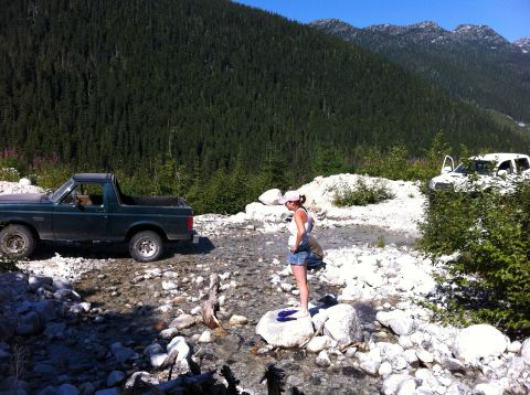 1990 Ford Bronco - Two vehicles are parked on a rocky trail in a mountainous, forested area with a woman standing nearby.