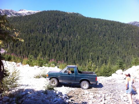 1990 Ford Bronco - A 1990 Ford Bronco is parked on a gravel road in a mountainous, forested area.