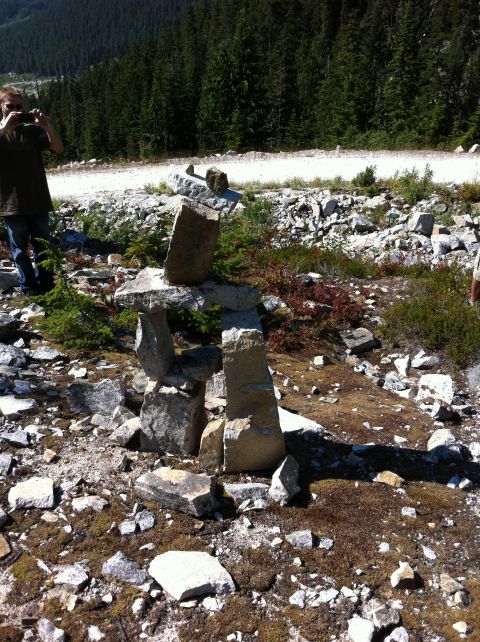 1990 Ford Bronco - A person stands on a rocky, wooded hillside, photographing a stacked stone inukshuk.
