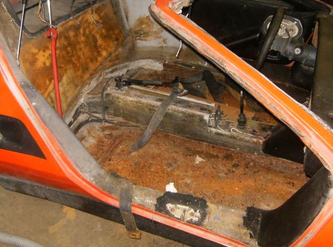 2000 Ford E350 - The interior of an orange vehicle shows significant rust damage on the floor and exposed components.