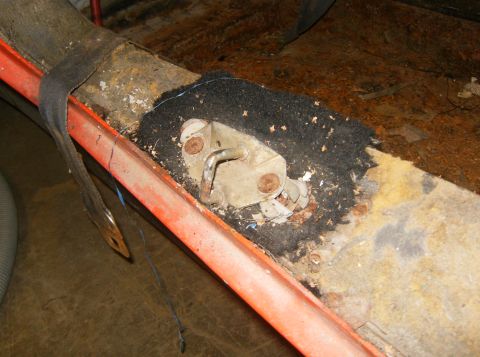 2000 Ford E350 - The interior floor of a vehicle shows a corroded door latch and worn seatbelt anchor.