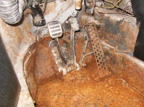 2000 Ford E350 - The interior floor of a vehicle shows significant rust around the brake and accelerator pedals.