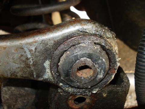 2000 Ford Crown Victoria - Close-up of a heavily worn and deteriorated rear control arm bushing, indicating a need for replacement.
