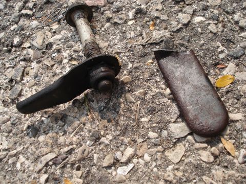 2000 Ford Crown Victoria - A close-up view of a damaged vehicle suspension part, possibly a control arm, resting on a gravel surface.