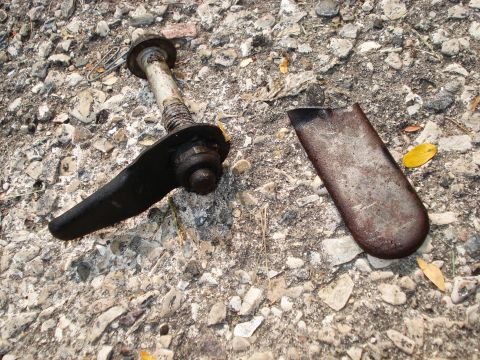 2000 Ford Crown Victoria - A damaged vehicle control arm and a separate metal piece lie on a gravel surface.