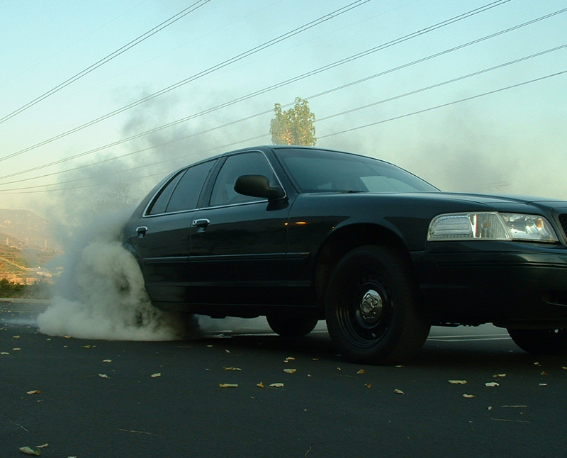 Black sedan doing a smoky burnout on a road