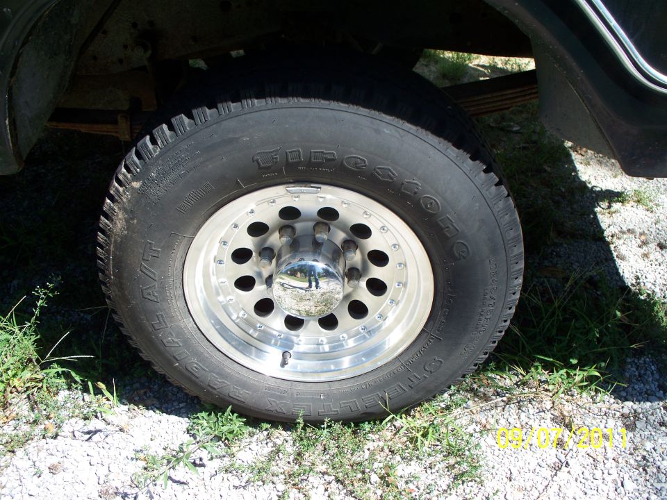 Close-up of a Firestone A/T radial tire on a polished aluminum wheel with a chrome hubcap