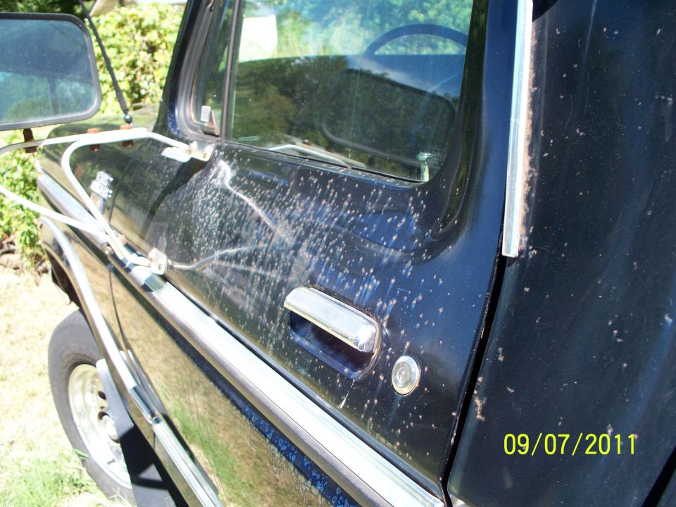 Black pickup truck door with chrome handle and side mirror, showing paint damage and water spots