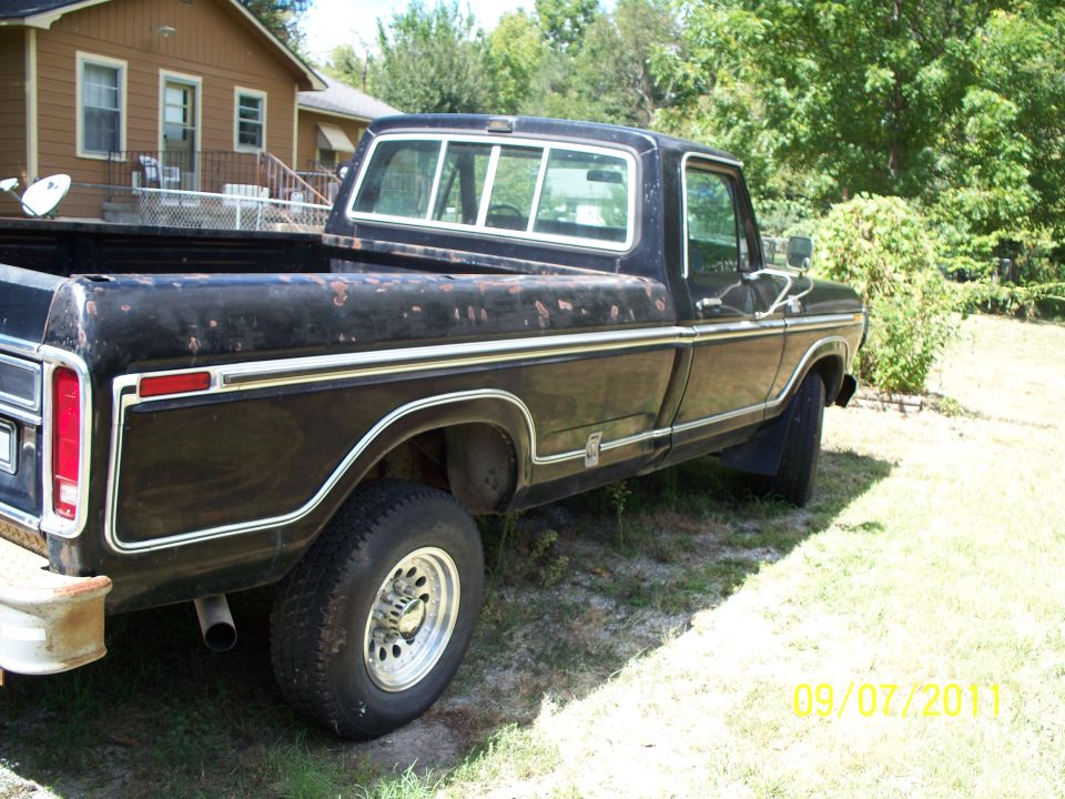 Faded black long-bed Ford F-Series pickup parked on grass with peeling paint and chrome trim