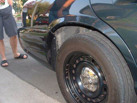 1998 Ford Crown Victoria - A close-up view of the rear wheel and fender of a dark-colored sedan.