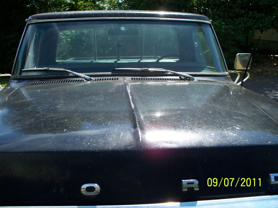 Front view of a black pickup truck hood and windshield. A "O" emblem is visible on the hood