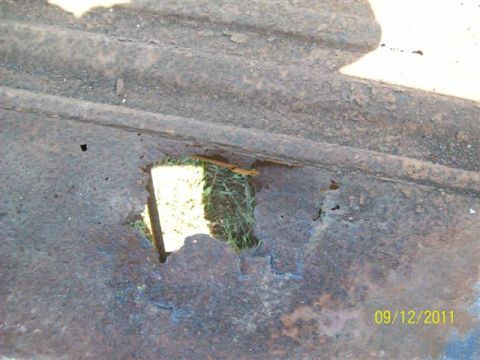 1979 Ford F-150 - Close-up of heavily rusted metal with a hole, showing grass and sky through the opening.