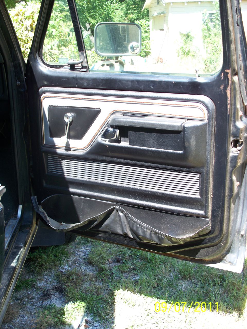 1979 Ford F-250 interior door panel with black trim, chrome handle, and a torn map pocket