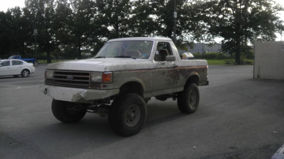 White Ford Bronco with aftermarket bumper and lifted suspension, covered in mud