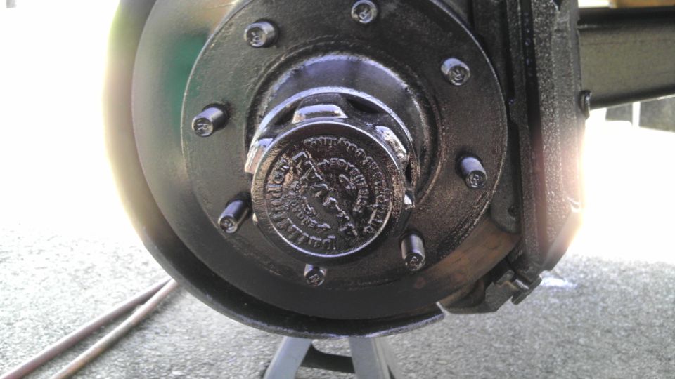 Close-up of a vehicle's front wheel hub with a brake rotor and caliper. The hub cap has some text and a logo on it