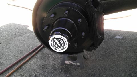 1989 Ford Bronco - Close-up of a vehicle's wheel hub and brake assembly, resting on a jack stand.